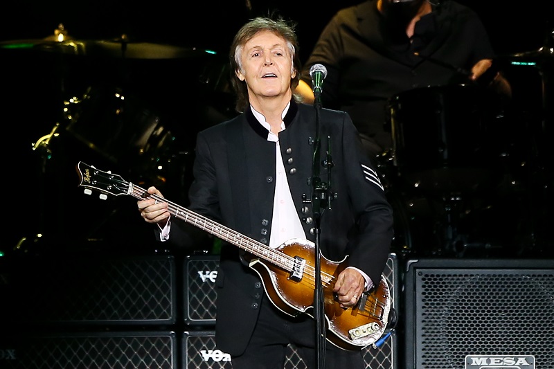 Paul McCartney, um dos maiores ícones do rock'n'roll, se apresentando em um palco, cantando e tocando baixo.