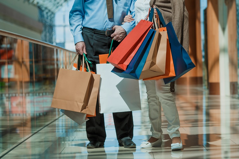 Duas pessoas caminham no shopping com uma sacola de compras. Imagem ilustra a matéria sobre como economizar com roupas na primavera.