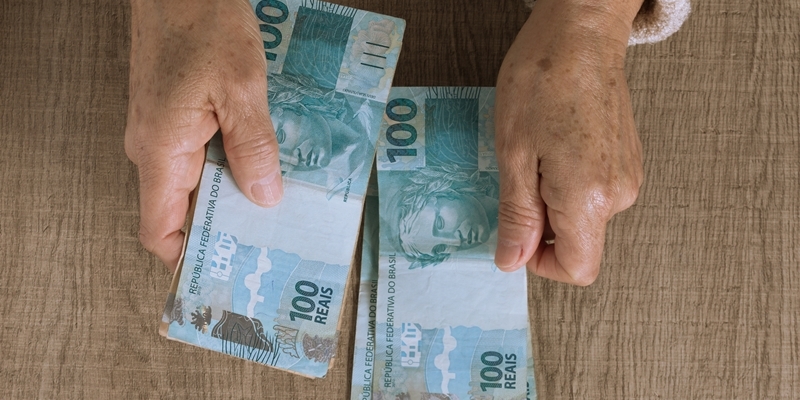 Uma senhora segurando notas de 100 reais. Imagem para ilustrar a matéria sobre 14º salário do INSS.
