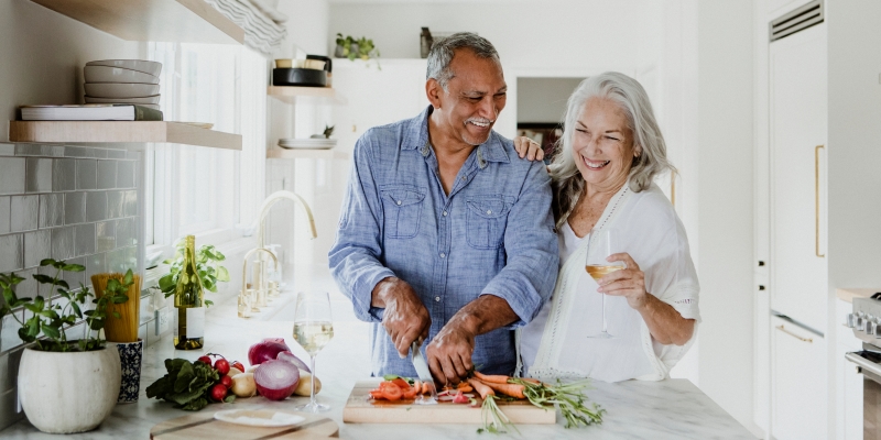 Um casal com 50+ cozinhando enquanto bebem vinho. Imagem para ilustrar a matéria sobre alimentação depois dos 50 anos.