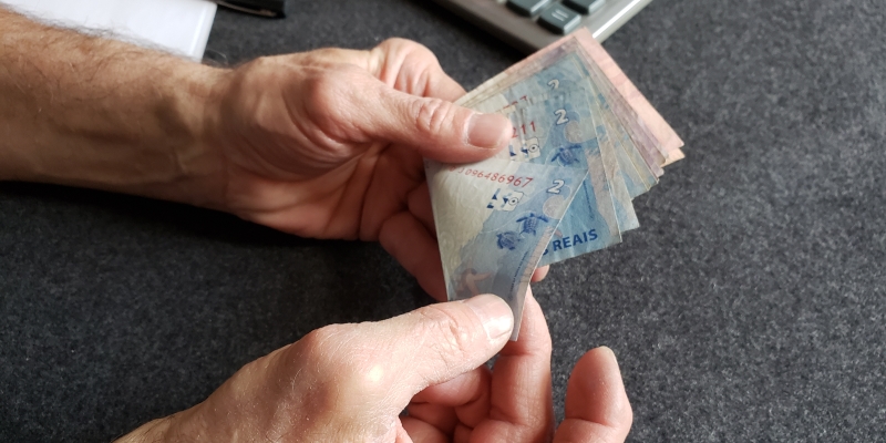 Um senhor segurando notas de dinheiro. Imagem para ilustrar a matéria sobre os benefícios de aposentados e pensionistas.