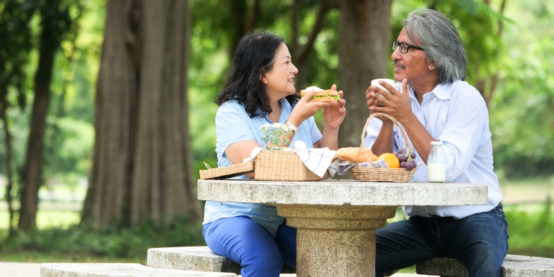 Um casal de senhores em uma praça fazendo um picnic. Imagem para ilustrar a matéria sobre economizar no verão.