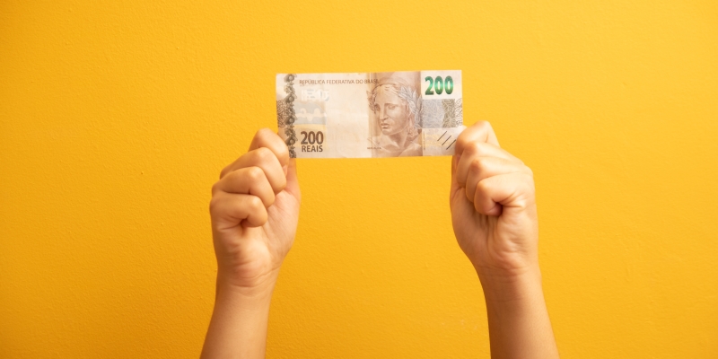 Uma mão segurando uma nota de R$200. Imagem para ilustrar a matéria sobre resgate do dinheiro esquecido.