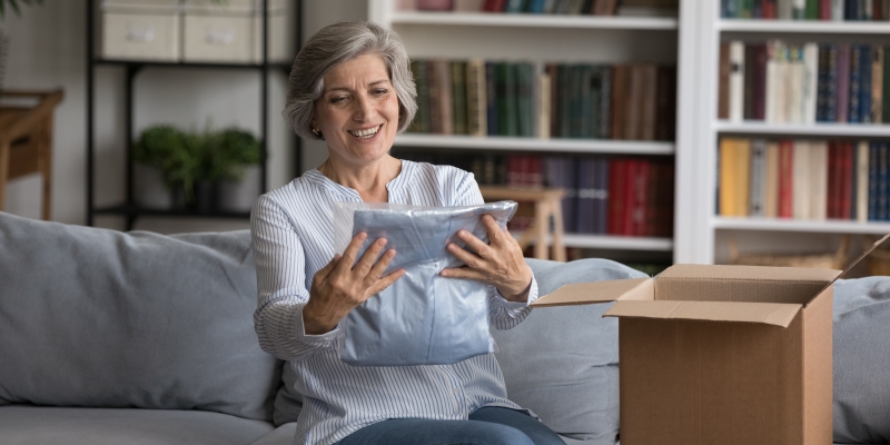 Uma mulher com expressão de felicidade após abrir uma caixa com compras enviadas pela internet. Imagem para ilustrar a matéria sobre gastar dinheiro é gostoso.