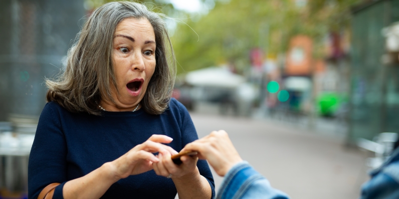 Uma mulher com uma expressão de desespero, tendo o celular roubado ou furtado no meio da rua por outra pessoa.