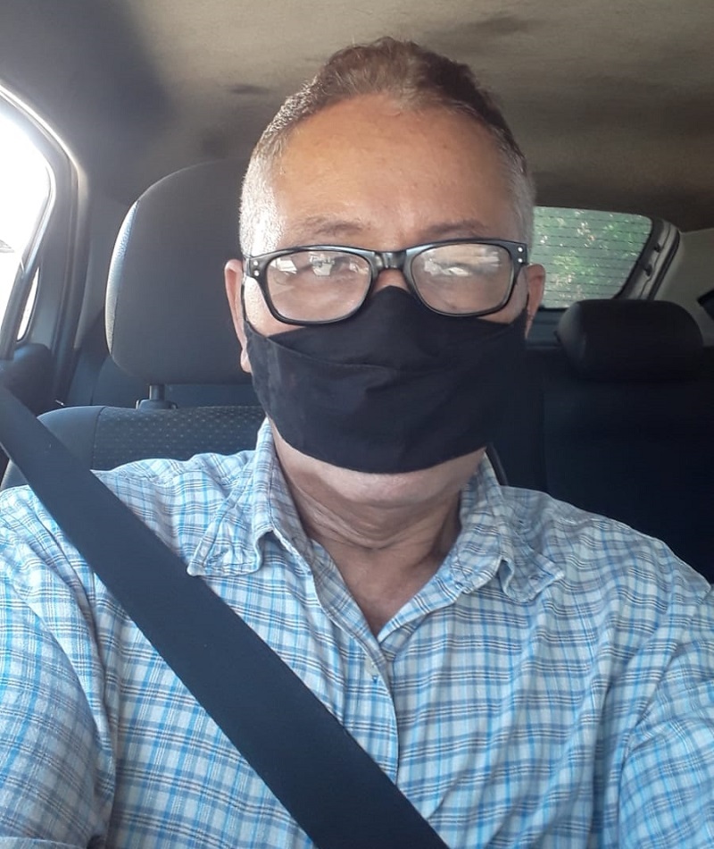 Givaldo sentado no banco da frente do carro, com cinto de segurança e máscara. Imagem para ilustrar a matéria sobre motorista de aplicativo.