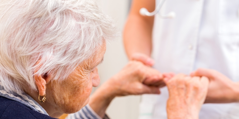 Uma senhora idosa segurando as mão de uma enfermeira. Imagem para ilustrar a matéria sobre quanto custa cuidar de uma pessoa com Alzheimer.