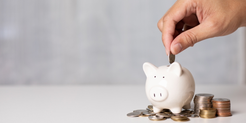 Uma pessoa colocando moedas em um porquinho. Imagem para ilustrar a matéria sobre poupar mais.