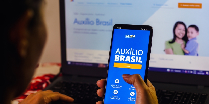 Uma pessoa com celular com o aplicativo do Auxílio Brasil aberto. A pessoa também está com o site do Auxílio Brasil aberto. Imagem para ilustrar a matéria sobre beneficiários do Auxílio Brasil.