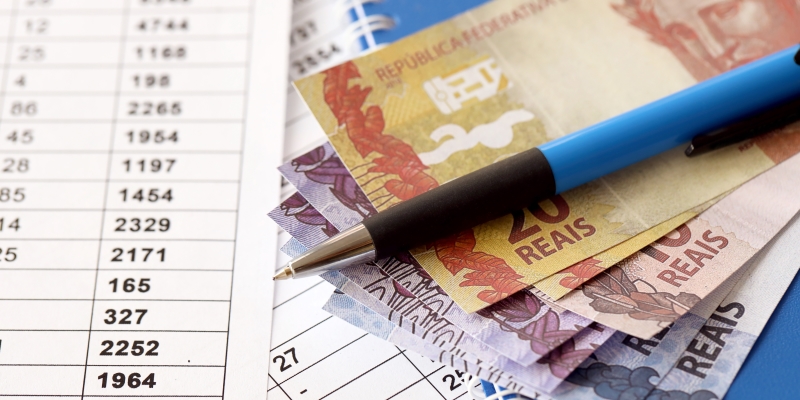 Uma tabela de cálculos, dinheiros e uma caneta. Imagem para ilustrar a matéria sobre o prazo  para quitação de empréstimos do Pronampe.