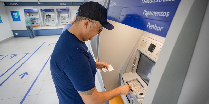 Um homem de meia idade sacando dinheiro em um caixa eletrônico dentro de um banco. Imagem para ilustrar a matéria de PIS/PASEP 2023.