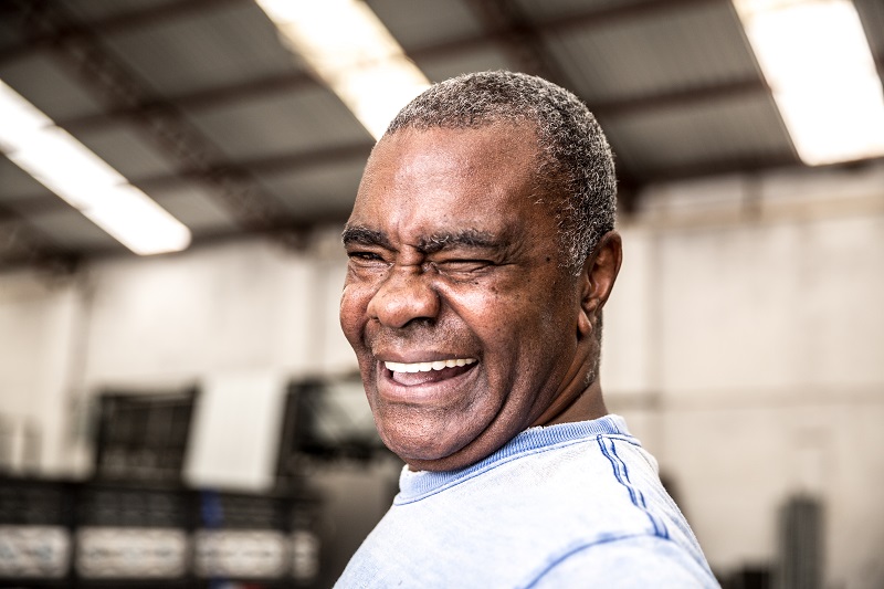 Como viver melhor: 15 hábitos para ter mais qualidade de vida no envelhecimento. Um homem negro com mais de 50 anos está com o rosto virado para a câmera e pisca um dos olhos, sorrindo.