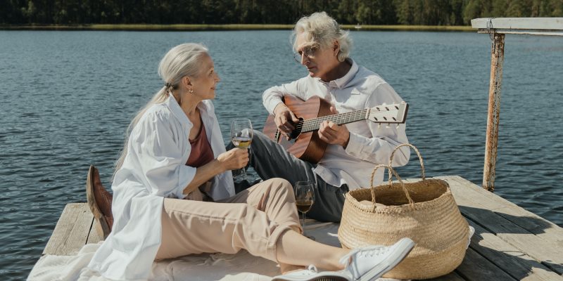 Um casal no deck de um lado. A mulher segura uma taça e o homem toca violão. Imagem para ilustrar a matéria sobre relacionamento duradouro.