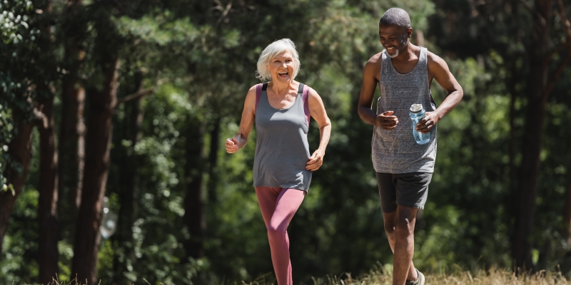 Um casal de idosos, sendo um homem negro e uma mulher branca, correndo em um parque. Imagem para ilustrar a matéria sobre conexão com a natureza.
