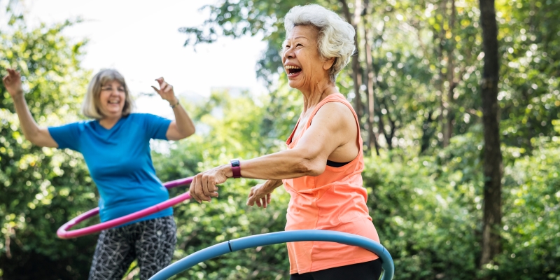 Duas mulheres idosas fazendo exercícios com bambolê. Imagem para ilustrar a matéria sobre envelhecimento feminino.