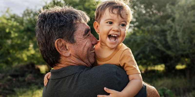 Avô brincalhão passando tempo com seu neto no parque em dia ensolarado. Imagem para ilustrar a matéria sobre o Programa de Benefícios ViverMais.