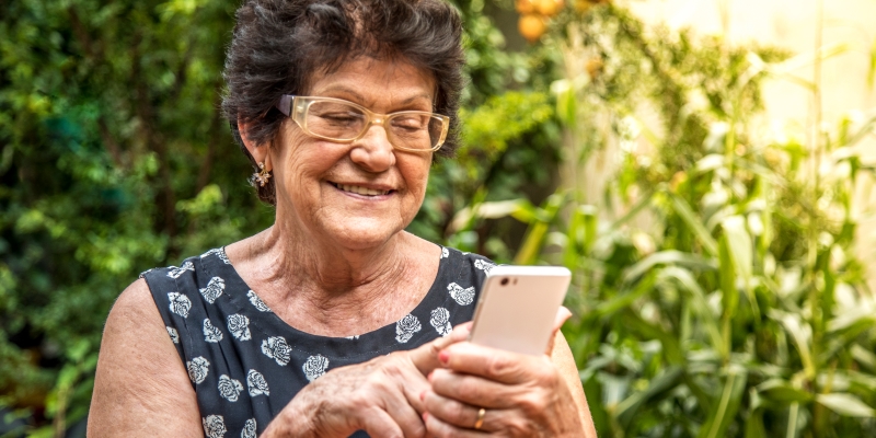 Mulher idosa feliz usando celular. Imagem para ilustrar a matéria sobre Programa de Benefícios ViverMais.