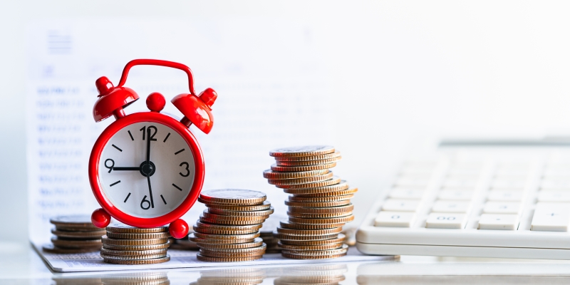 Um monte de moedas ao lado de um mini relógio sobre uma mesa. Imagem para ilustra a matéria sobre aposentadoria privada.
