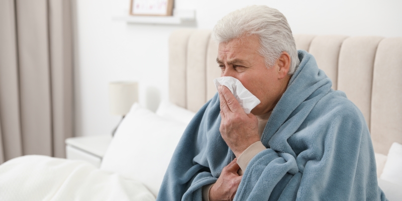 Homem sofrendo de frio em casa e assoando o nariz, por conta de doenças respiratórias.