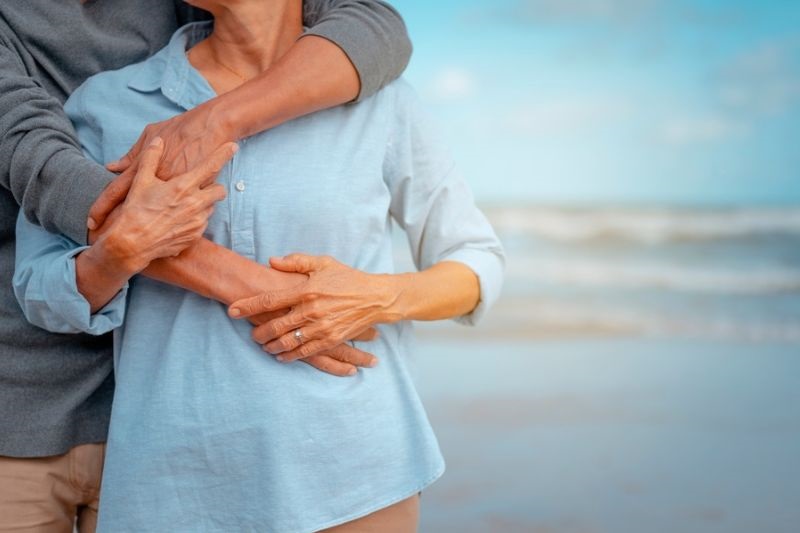 Um casal de idosos se abrançando em uma praia. Seguro de vida e assistência funeral são ferramentas de proteção