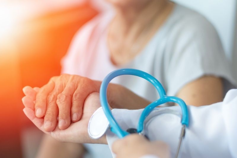 Uma senhora idosa segurando a mão de uma profissional de saúde. Imagem para ilustrar a matéria sobre planos de saúde para os 60+.