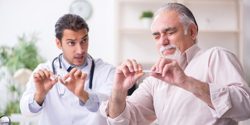 Um homem de 50 anos em frente a um médico, dentro do consultório, quebrando um cigarro. Imagem para ilustrar a matéria sobre hábitos saudáveis para viver mais.