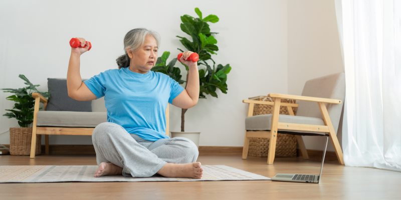 Um mulher fazendo exercicios vendo vídeo no computador. Imagem para ilustrar a matéria sobre como manter uma rotina de exercícios depois dos 50 anos.