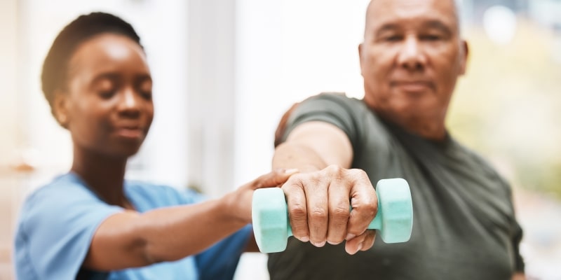 Um senhor mais velho fazendo musculação com uma fisioterapeuta dando suporte. Imagem para ilustrar os pilares para envelhecer bem.