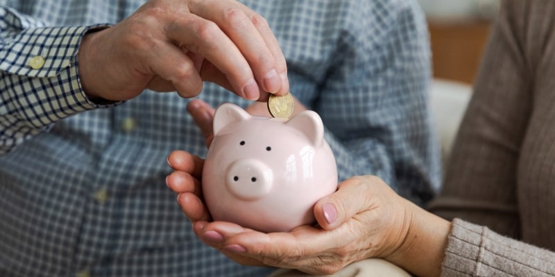 Um casal de idosos guardando dinheiro em um cofrinho de porco para controlar as finanças.