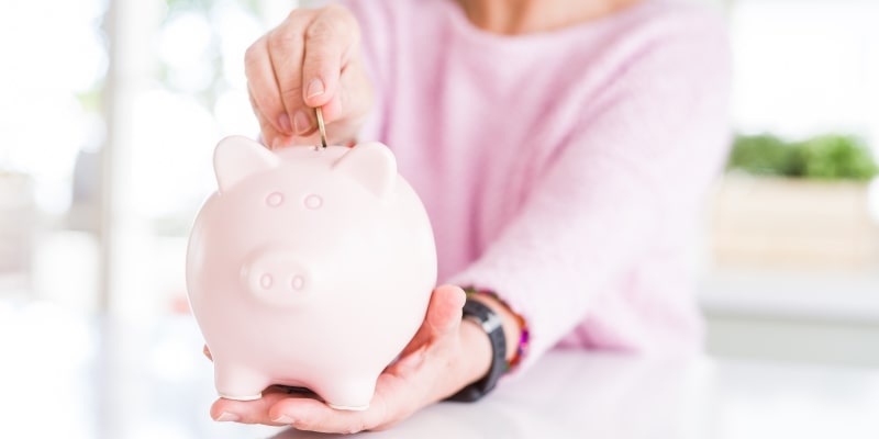 Uma mulher guardando dinheiro em um cofre de porco. Imagens para ilustrar a matéria sobre dinheiro da aposentadoria.