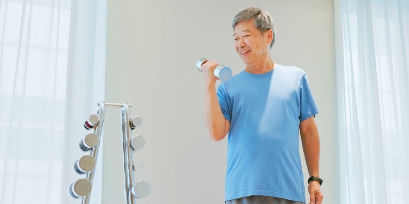 Um homem asiátivo com cerca de 40 anos fazendo musculação ao levantar um peso de mão.