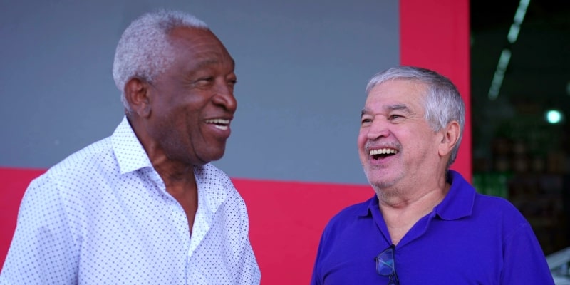 Dois idosos, sendo um homeme branco e um homem negro, rindo na rua, ao conversar. Imagem para ilustrar a matéria sobre recorde de envelhecimento.