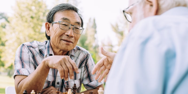 Dois idosos, sendo um asiático e um caucasiano, jogando xadrez em uma praça. Imagem para ilustrar a matéria sobre descobertas sobre a longevidade.