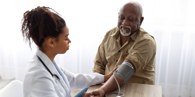 Um senhor negro de idade verificando a pressão com uma enfermeira negra jovem. Imagem para ilustrar a matéria sobre medicina preventina.