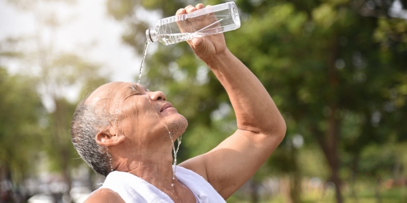Um idoso jogando água de uma garrafa pet no rosto. Imagem para ilustrar a matéria sobre onda de calor excessivo.