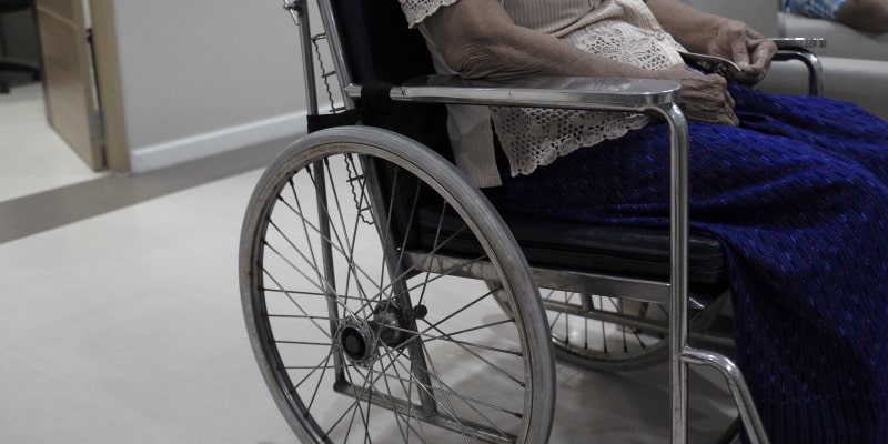 Uma senhora idosa sentada em uma cadeira de rodas em um hospital. Imagem para ilustrar a matéria sobre o sistema de saúde brasileiro.