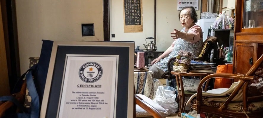 Tomoko Horino, a consultora de beleza mais velha do mundo, em sua casa apontando para o quadro do Guinness, com sua premiação.