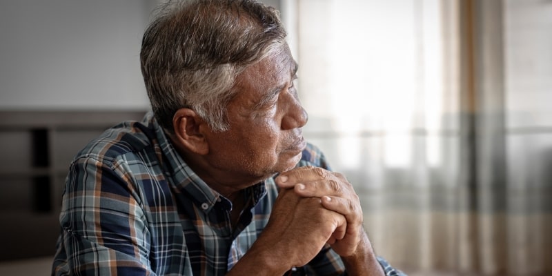 Um homem idoso triste, com as mãos no queixo, olhando para o horizonte. Imagem para ilustrar a matéria sobre envelhecimento masculino.