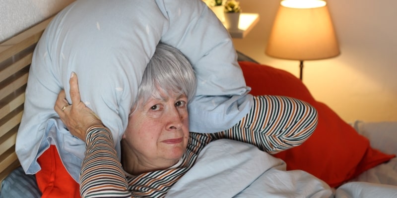 Mulher idosa sem dormir cobrindo os ouvidos com travesseiro por causa dos fogos de artifício.
