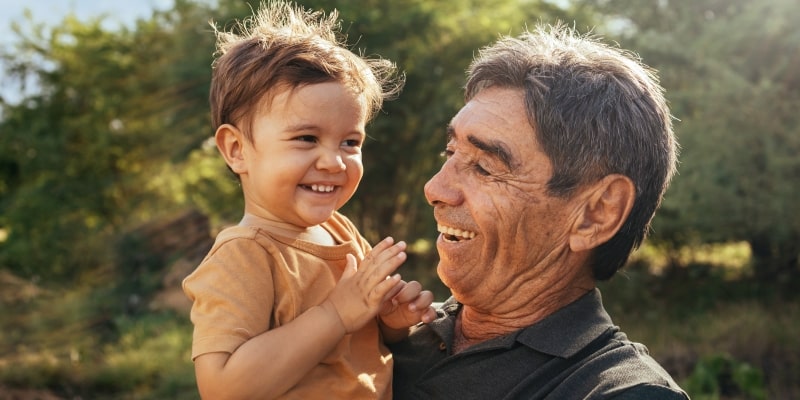 Avô brincalhão passando tempo com seu neto no parque em dia ensolarado. Imagem para ilustrar a matéria sobre a satisfação com o envelhecimento.