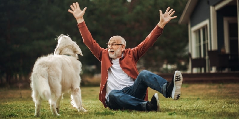 Homem idoso alegre, aproveitando o tempo fora de casa, em um quintal, com um cachorro de estimação. Imagem para ilustrar a matéria sobre cuidar de cães.