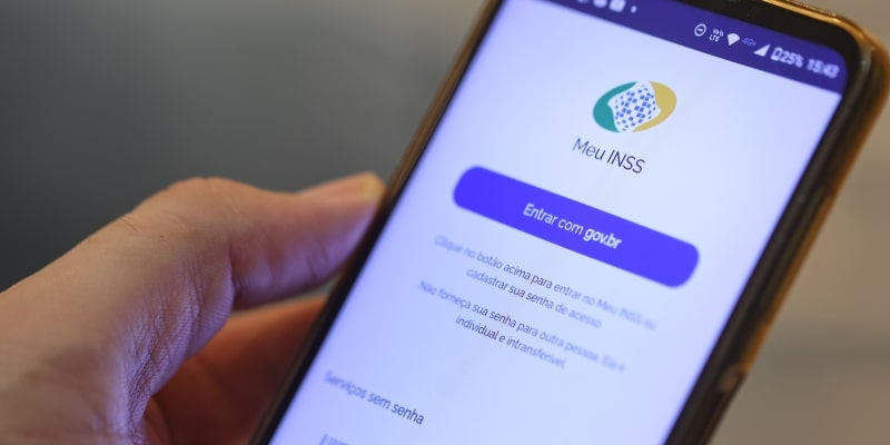 O aplicativo do INSS na tela de um celular que um homem está segurando. Imagem para ilustrar a matéria sobre extrato da aposentadoria com reajuste.