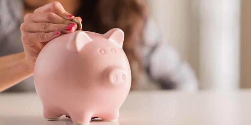 A mão de uma mulher colocando uma moeda em um cofrinho de porco. Imagem para ilustrar a matéria sobre dinheiro acaba antes do fim do mês.