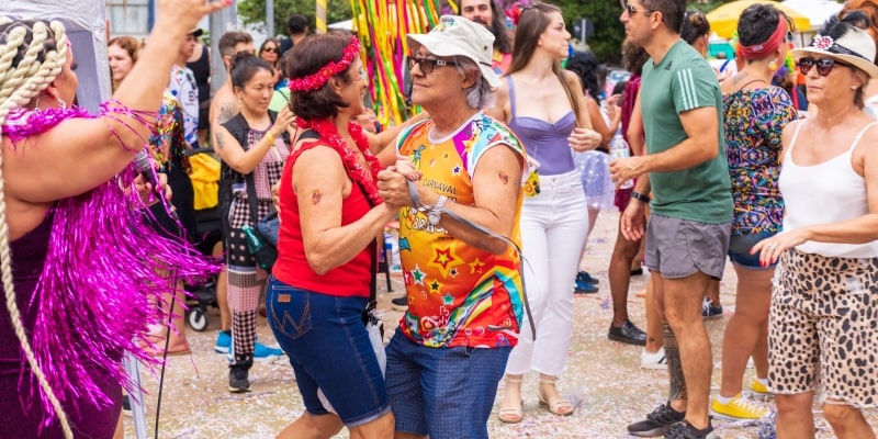 Um casal idoso dançando junto em um bloco de carnaval de rua. Imagem para ilustrar a matéria sobre preservativos.