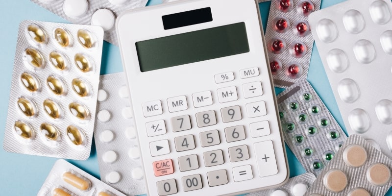 Um calculadora. Ao redor dela, diversas cartelas de remédios. Imagem para ilustrar a matéria sobre custo de medicamentos.