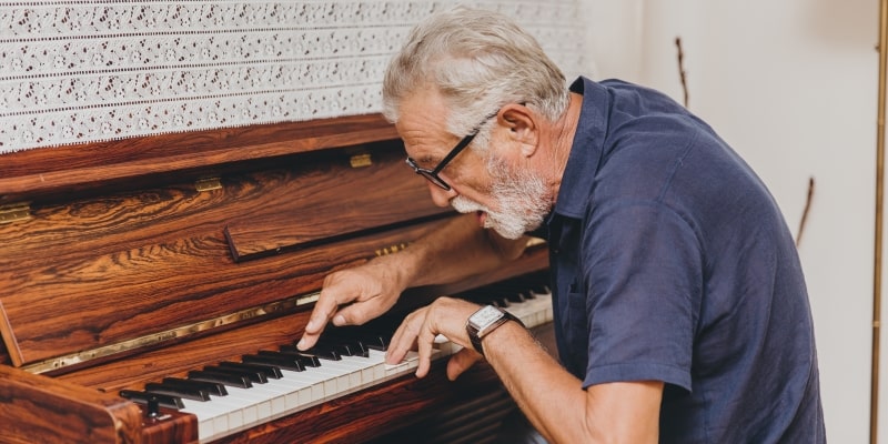 Um homem idoso com alguma demência tocando piano. Imagem para ilustrar a matéria sobre como a música pode ajudar idosos.