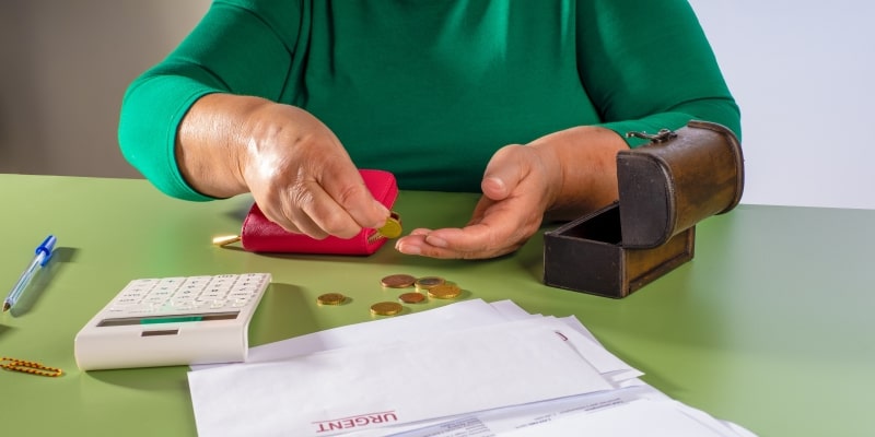 Mãos de uma mulher idosa contando moedas. Em sua frente em uma calculadora e contas urgentes. Imagem para ilustrar a matéria sobre fazer um empréstimo consignado.
