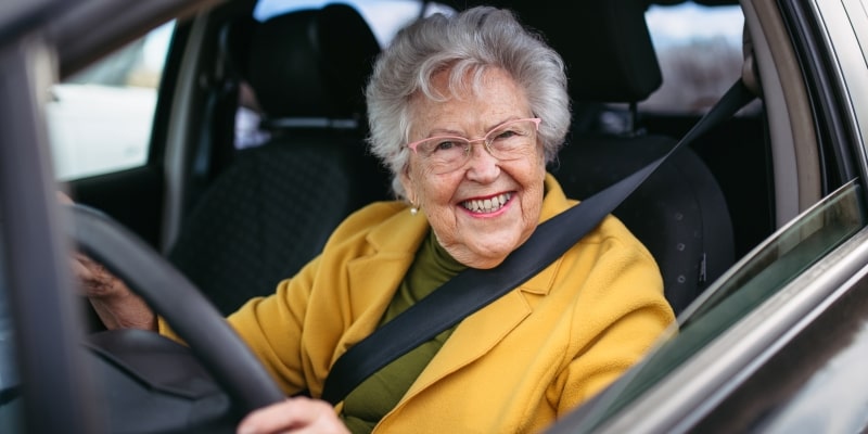 Uma senhora dirigindo e sorrindo. Imagem para ilustrar a matéria sobre a nova lei da CNH para idosos.
