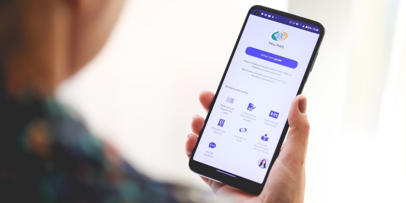 Uma mulheres segurando um telefone e usando o aplicativo Meu INSS. Imagem para ilustrar a matéria sobre o Atestmed do INSS.