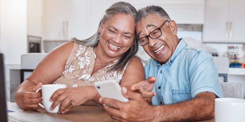 Um casal sorrindo enquanto olham para o celular, vendo os benefícios que garantem qualidade de vida para os idosos.